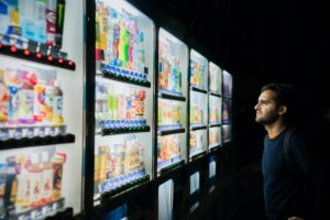 La imagen destacada de este texto muestra del lado derecho a un hombre observando luna serie de refrigeradores iluminados que contienen diferentes productos; es decir, esta frente a la competencia económica en vivo.