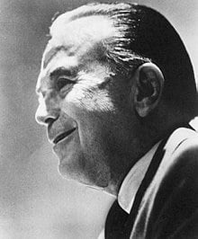 Esta es una fotografía en blanco y negro de perfil del emprendedor Ray Kroc; hombre mayor, sonriente, vestido de con saco oscuro.