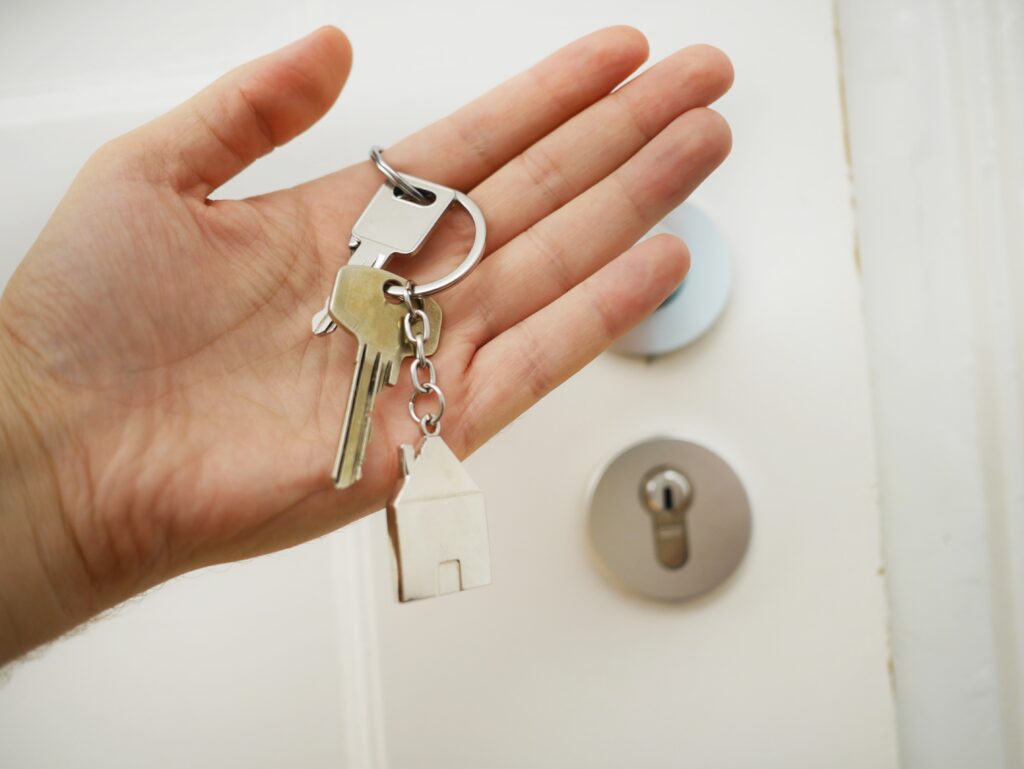 La imagen destacada sobre este texto de mitos y realidades del Infonavit, muestra una mano extendida que carga un par de llaves con un llavero metálico de una casa. De fondo se aprecia una puerta blanca con cerradura metálica.