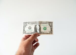 Como imagen destacada de este texto sobre Jerome Powell, presidente de la FED y la inflación que vive EU tenemos una fotografía de una mano que sostiene un billete de un dólar extendido, sobre un fondo blanco.