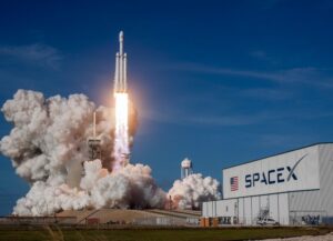 Para este texto sobre cinco trabajadores que fueron despedidos de SpaceX, empresa fundada por Elon Musk, tenemos una fotografía en la que vemos el despegue de uno de sus cohetes, junto a una planta donde se lee el nombre de la empresa.