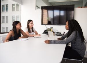 Para este texto sobre consejos para prepararse antes de una entrevista laboral tenemos una imagen destacada en la que hay 3 mujeres en una sala de juntas; dos están sentadas frente a la mesa del centro, en el lado izquierdo de la pantalla, al frente está una tercera.