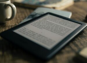 La imagen destacada de este texto sobre la salida de Kindle, tienda de libros de Amazon, de China, es una fotografía de un dispositivo de Kindle, es decir un libro electrónico, que se encuentra encendido, sobre una mea de madera.