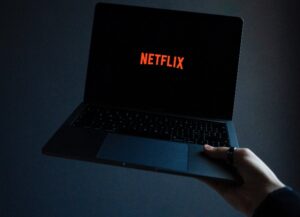 Netflix pierde casi un millón de suscriptores; como imagen destacada para nuestra nota al respecto tenemos una fotografía en la que una computadora portátil es sostenida de su esquina inferior derecha y muestra su pantalla en la portada de inicio para ingresar con netflix: fonoteca negro y letras en rojo.