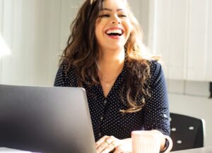 Como imagen destacada para este texto titulado: Condusef ofrece Diplomado en Seguros gratuito y en línea, tenemos la fotografía de una mujer sonriente, frente a su computadora portátil.