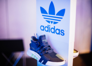 Como imagen destacada para este texto titulado: Kasper Rorsted, CEO de Adidas, se despide de la firma tenemos una fotografía del logo en una stand blanco arriba de una zapatilla deportiva.