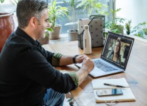 Como imagen destacada para esta nota de que Google promete unir sus servicios de reuniones virtuales tenemos una fotografía de un hombre sentado frente a una mesa de trabajo con su computadora portátil en un videollamada.