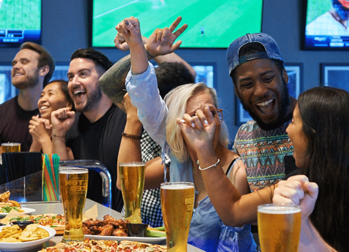 Como imagen interna tenemos una fotografía de un grupo de amigos sentados alrededor de una meza de Boston's-Pizza, disfrutando del ambiente del bar deportivo o sports bar.