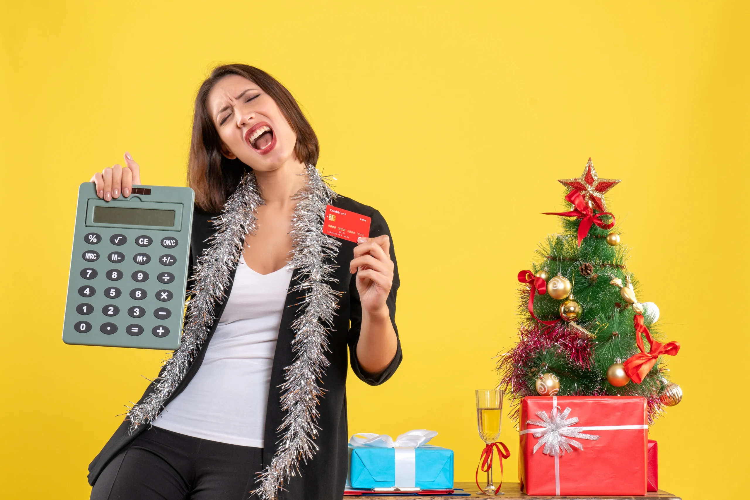 Como imagen destacada para este texto en el que hablamos del aguinaldo de 40 días, tenemos una imágen ilustrativa de una mujer frente a un árbol de Navidad con una tarjeta de crédito y una calculadora en las manos. 